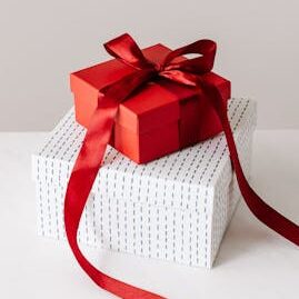 From above of wrapped with ribbon red square gift box placed on white with silver little rhombuses square box on white table against gray background
